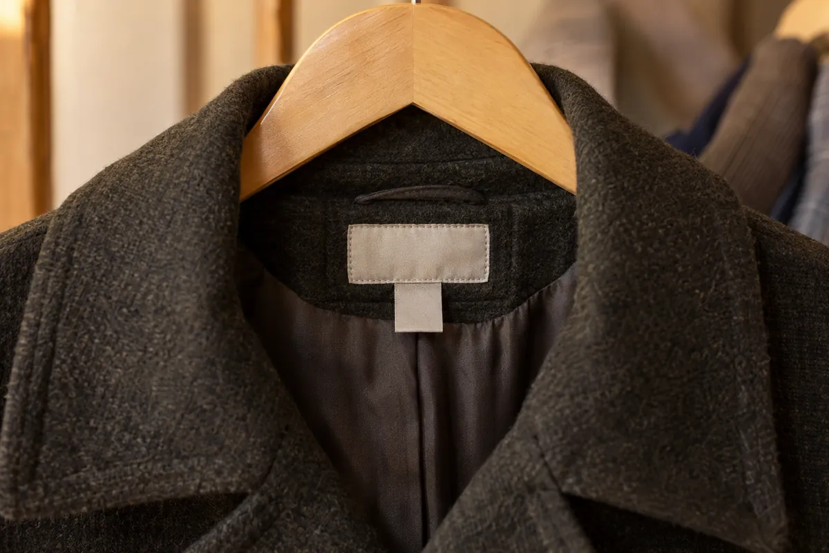 The inside collar of a wool coat showing its sewn labels
